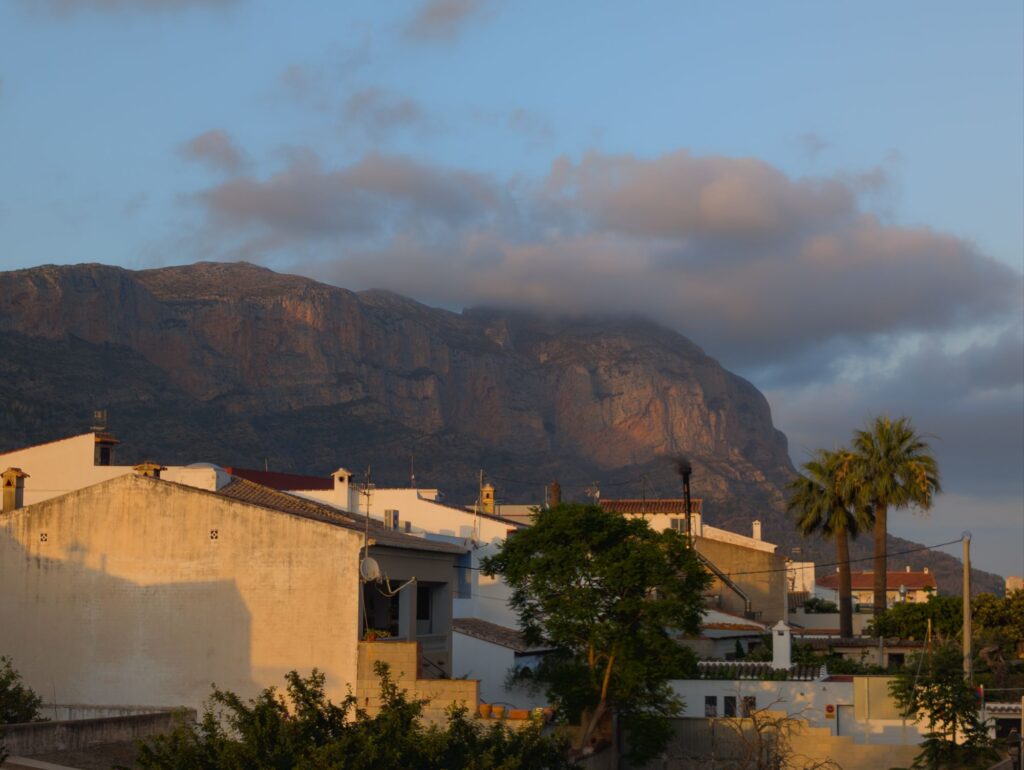 Traditional Spanish village houses with terracotta roofs set against the imposing limestone cliffs of Montgó mountain in the evening light