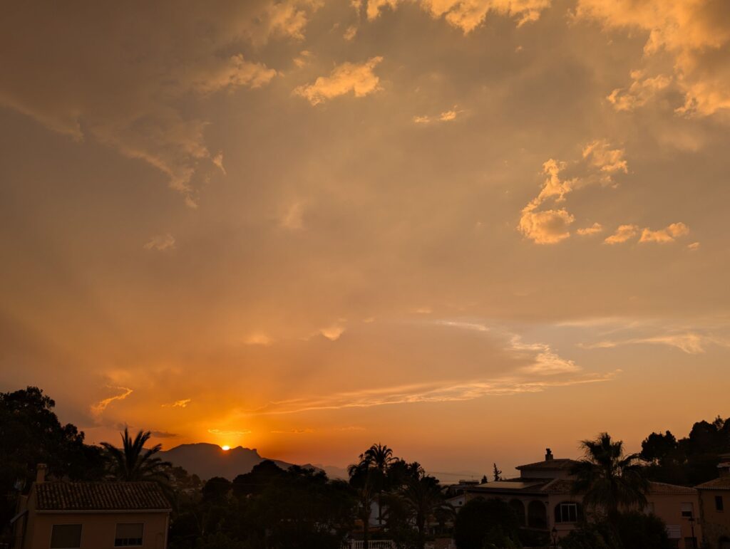 Golden sunset over village rooftops with palm trees silhouetted against the dramatic orange and yellow sky
