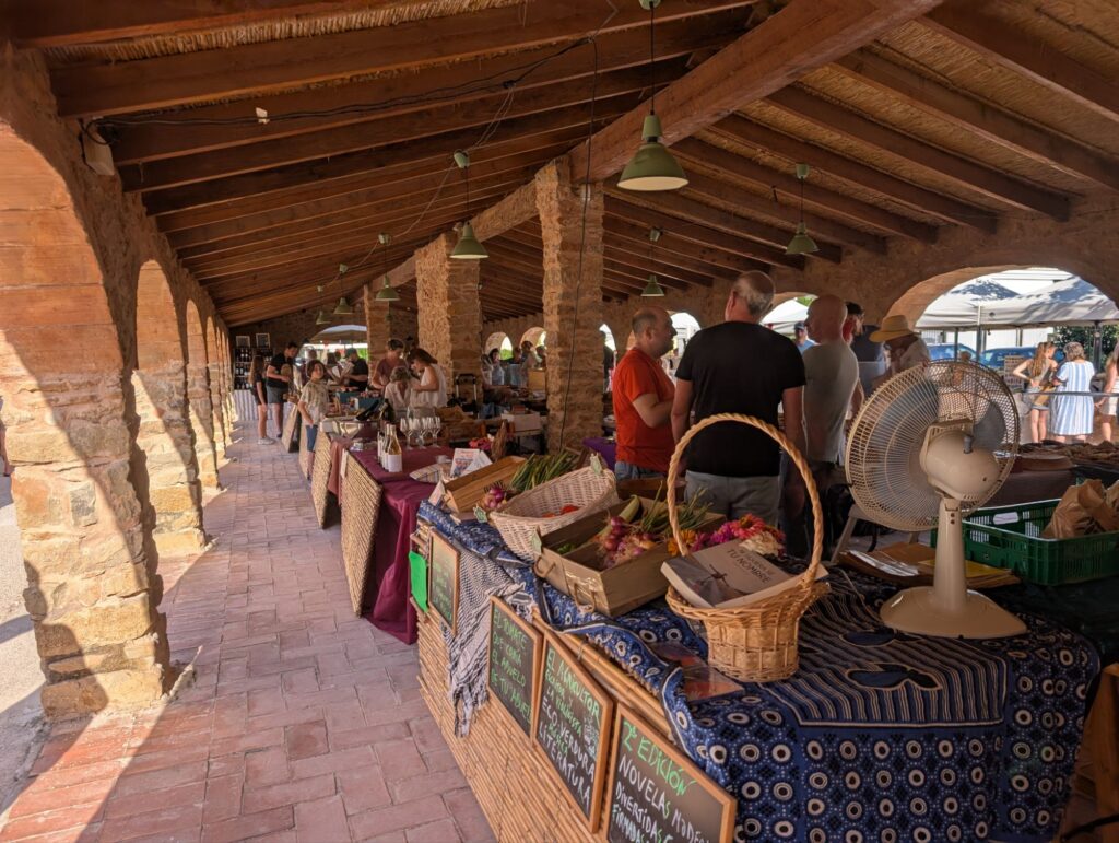 Market stalls set up under the traditional stone arches of the Riurau building, with vendors selling local produce and crafts