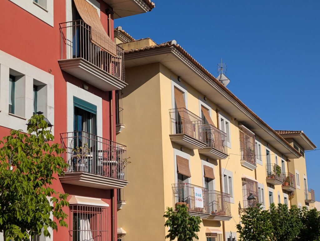 Row of multi-storey Spanish houses painted in yellow, pink and cream colours with decorative iron balconies and flower boxe