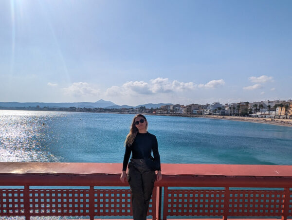 A picture of Caitlin, the Editor of Explore Costa Blanca Spain, with the Javea Port Beach in the background on a sunny day